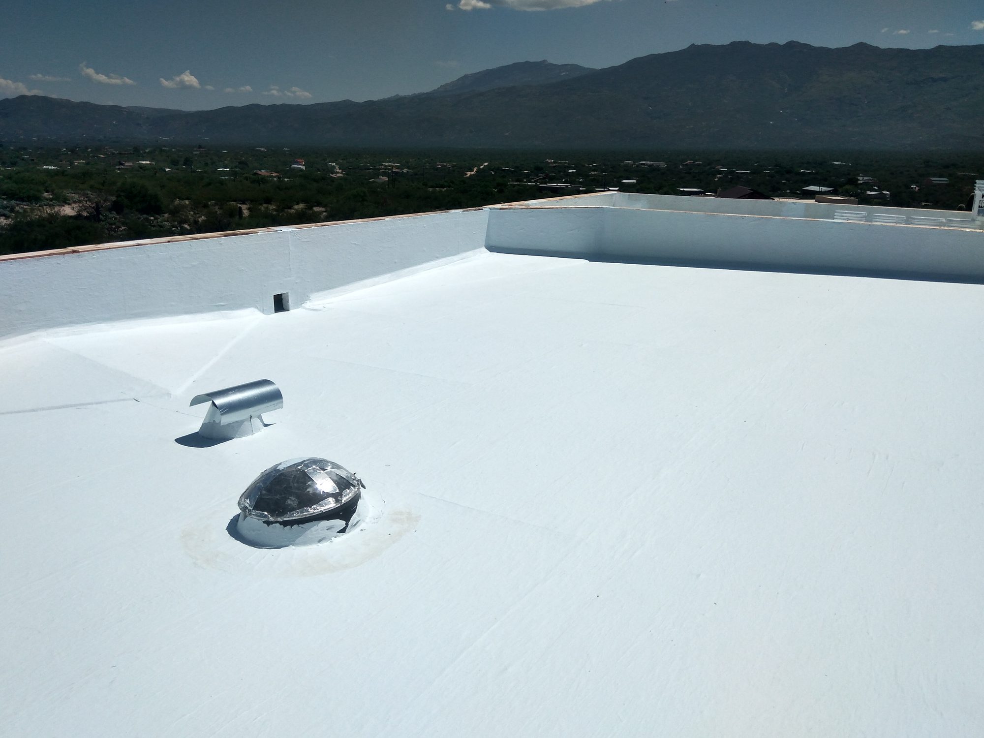 Restored flat roof finished in white coating with the Rincon Mountains on the horizon, Tucson