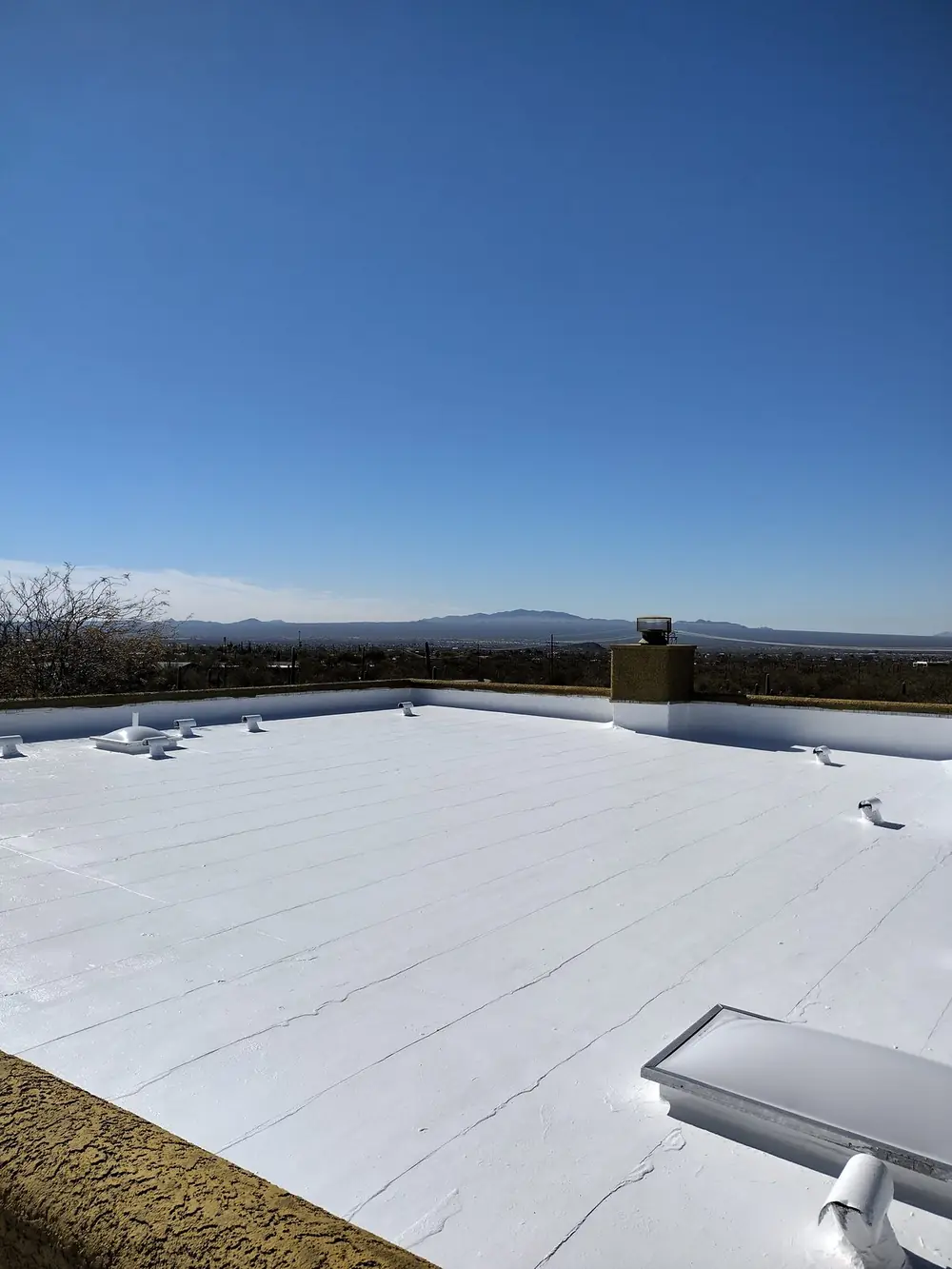 Low-sloped Tucson roof finished in white premium-grade acrylic coating with mountains on the horizon