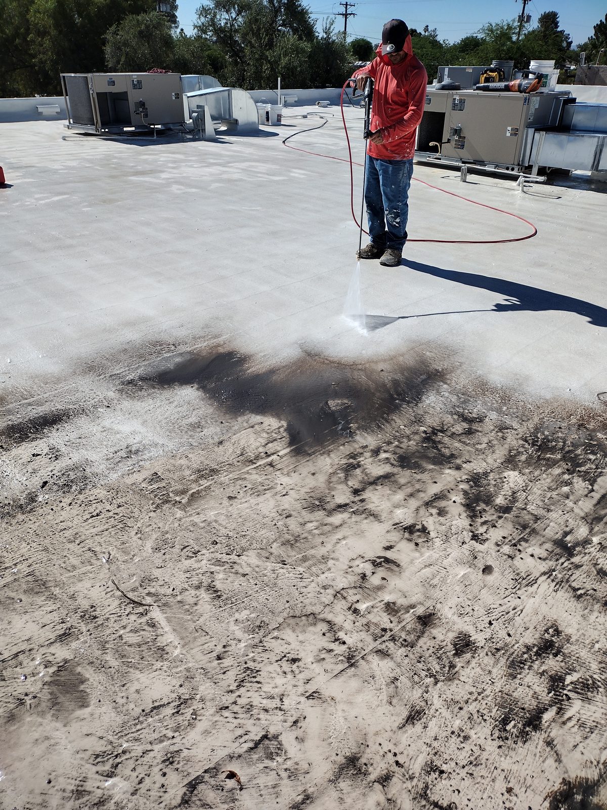 Pressure washing a Tucson flat roof, showing the cleaned surface next to the untouched section