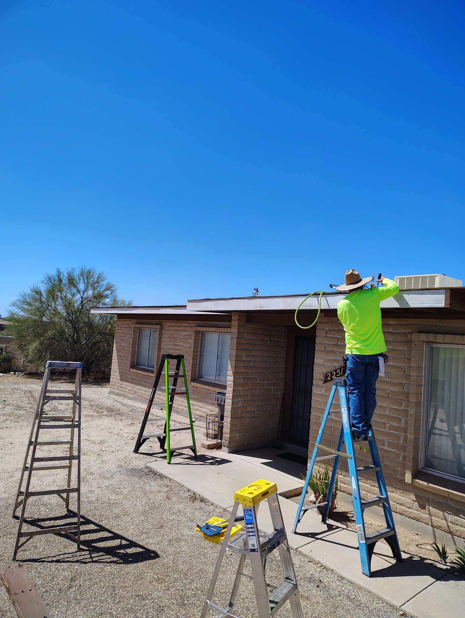 Pro Roof LLC crew working from ladders on a low-sloped roof at a Tucson home